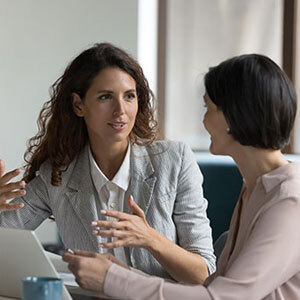 Two professional women are sitting at a table with a laptop, engaged in negotiation with a seller