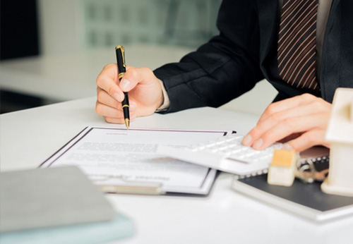A close-up view of a person’s hand signing a legal contract or settlement agreement with a fountain pen on a desk.